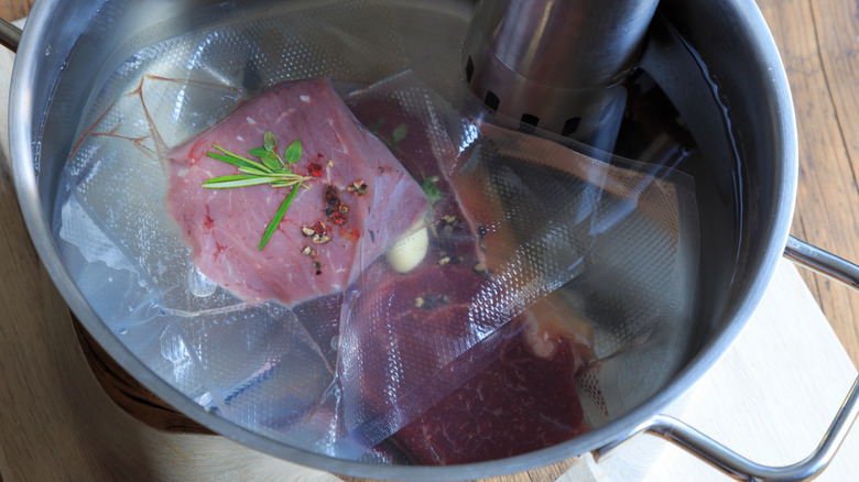Meat vacuum sealed in sous vide bags in a large pot with water next to a sous vide machine.