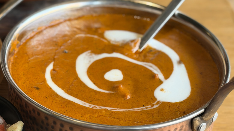 A pot full of butter chicken with a large spoon partially submerged into it