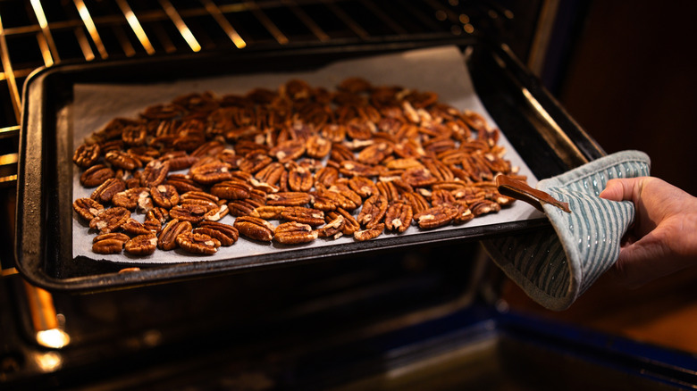 Hand putting pan of pecans in oven