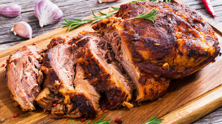 Seasoned pork shoulder with pieces torn off of it on a wooden serving board