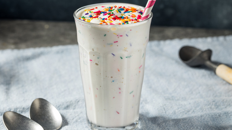 Glass of milkshake with rainbow sprinkles on top and a straw