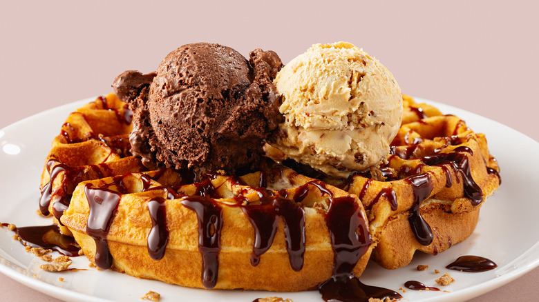 A large waffle with two scoops of ice cream and chocolate syrup on it