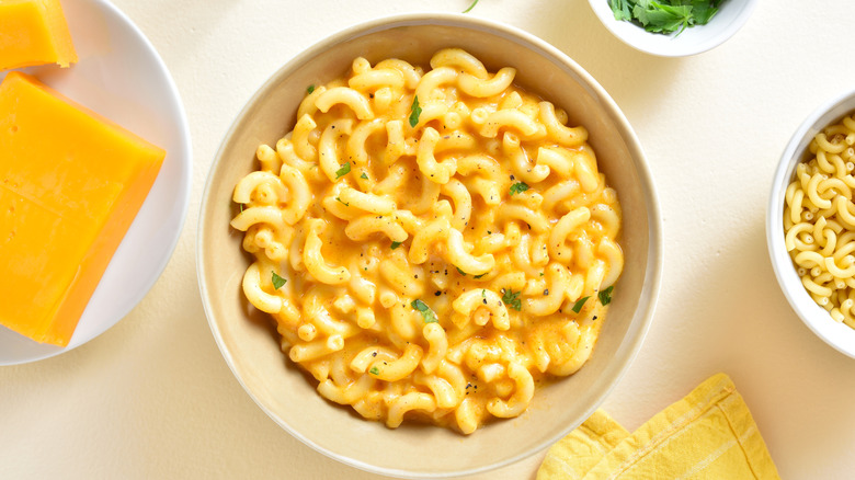 Overhead of cheesy macaroni and cheese in a bowl near bowls of cheese and uncooked pasta.
