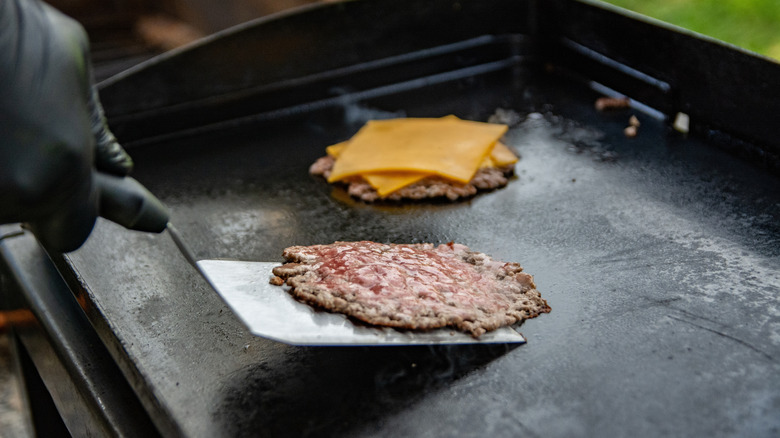 A chef flips a smash burger patty on a grill
