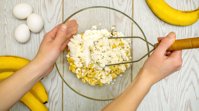 Overhead view of hands mashing cottage cheese into banana in a bowl