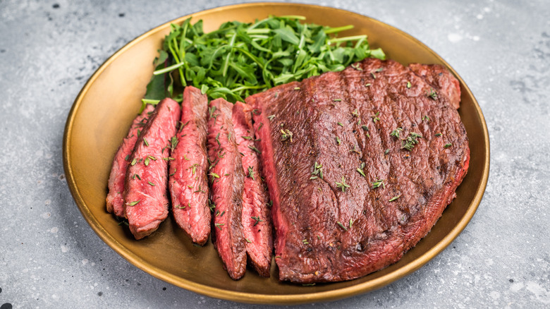 Sirloin steak cooked to medium with arugula salad on plate.