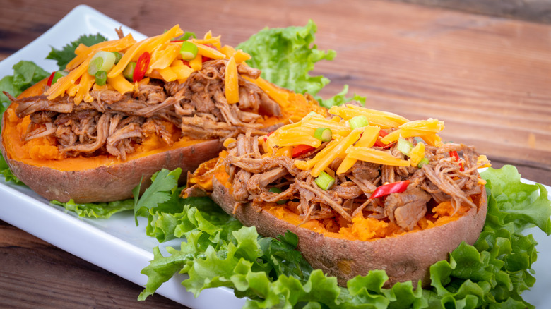 Two halves of sweet potatoes stuffed with pulled pork on bed of lettuce