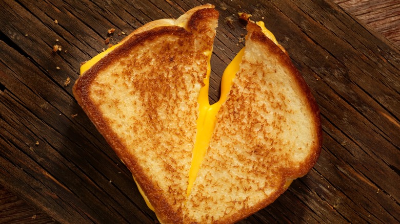 Grilled cheese sandwich cut in half and oozing cheese on wood surface.