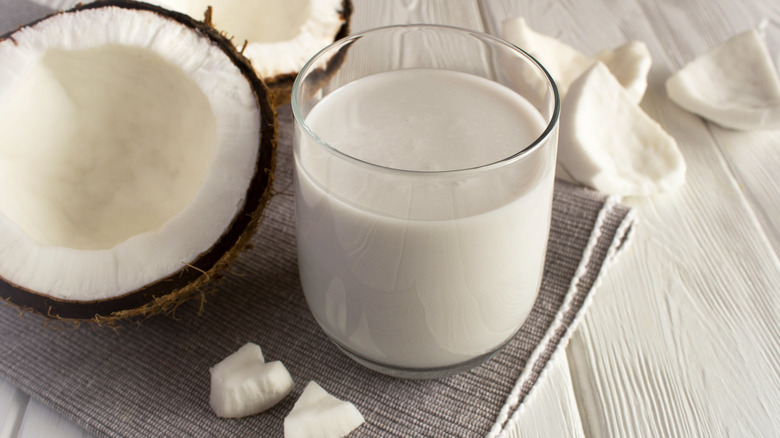 A small glass of coconut milk beside an opened coconut with coconut flesh nearby