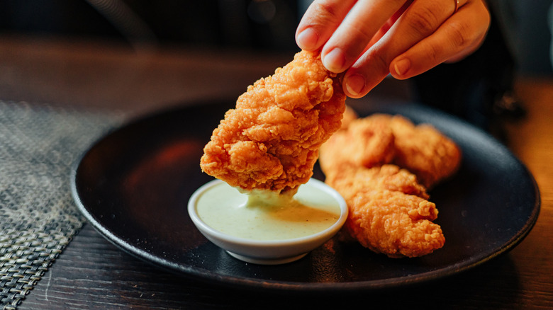 A hand dipping a chicken tender into sauce