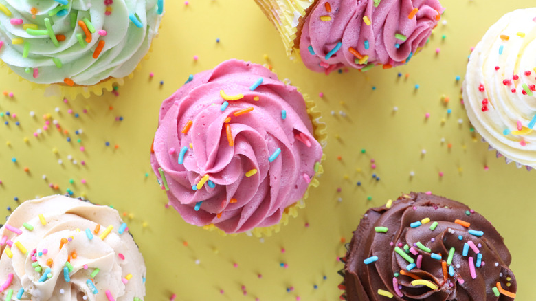 Top view of cupcakes with pink, brown, white, or light green frosting and multi-colored sprinkles