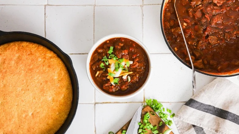 Bowl of brisket chili with cornbread, toppings, and pot of chili