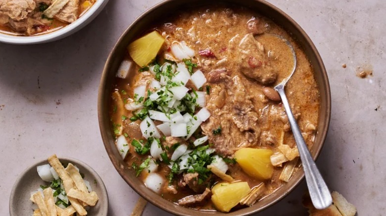 Bowl of tacos al pastor pork chili with a spoon, topped with onion and pineapple