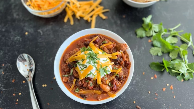 Bowl of Italian sausage chili with spoon, cilantro, and cheese