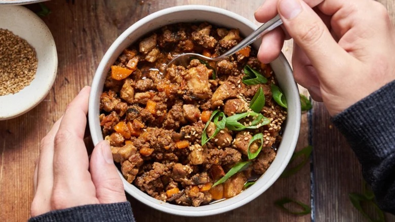 Hands holding bowl of beef and pork chili with a spoon