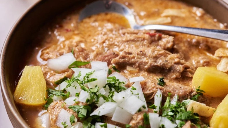 Bowl of tacos al pastor pork chili with spoon and topped with onion
