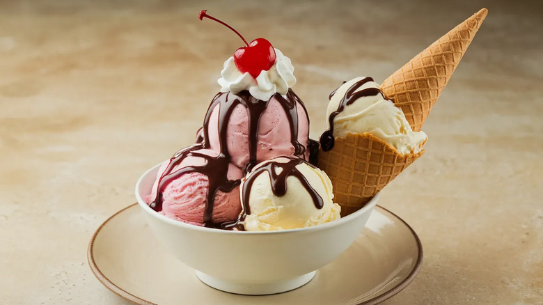 A bowl of an ice cream sundae with several scoops, a waffle cone, and a cherry on top.