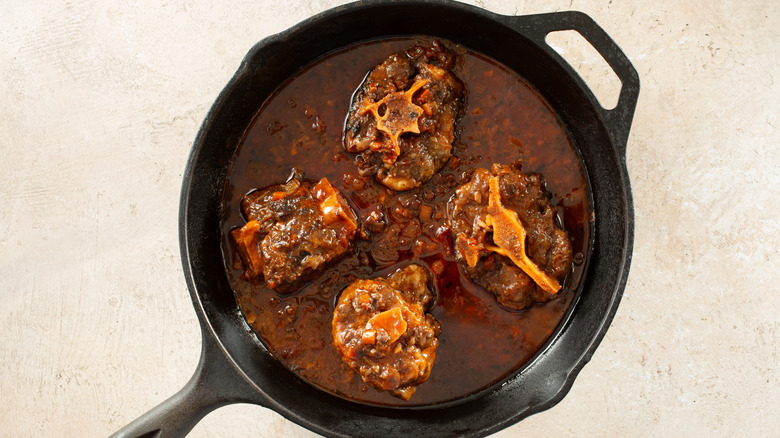 Four pieces of oxtail braising in a cast iron skillet