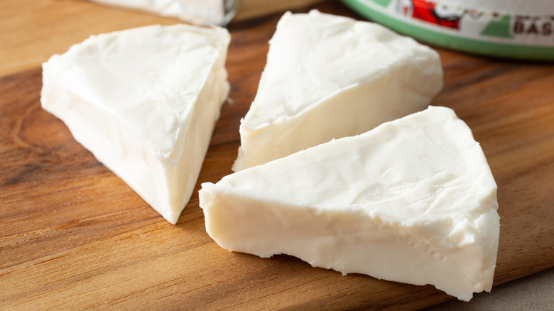 Spreadable cheese wedges next to packaging on cutting board.