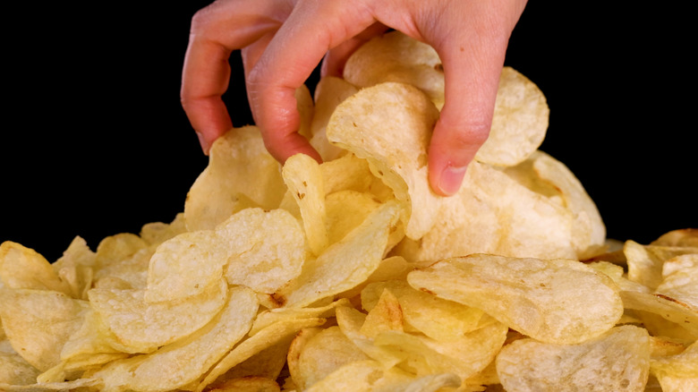 Hand grasping giant mount of potato chips on black background.