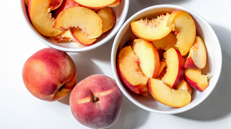 Whole peaches next to bowls of sliced peaches