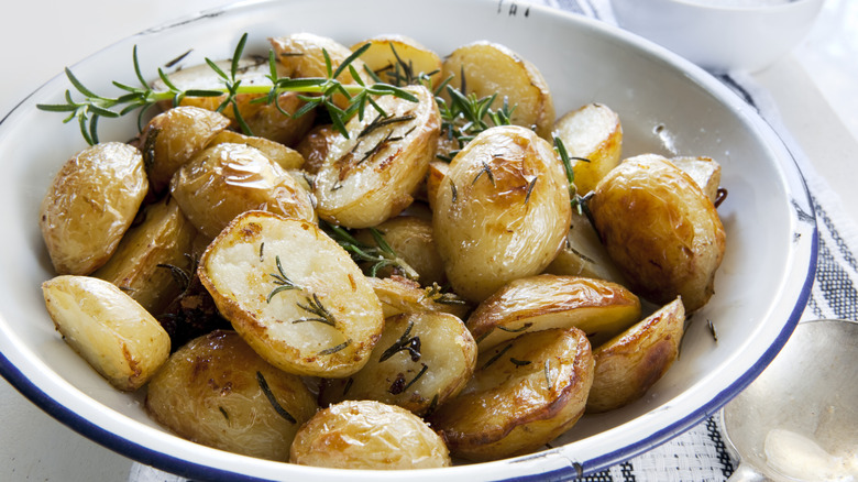 Top view of roasted potatoes with rosemary served in a white plate on clothed table.