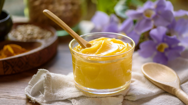 Ghee butter in glass jar with wooden spoon on wooden table with blurred background.