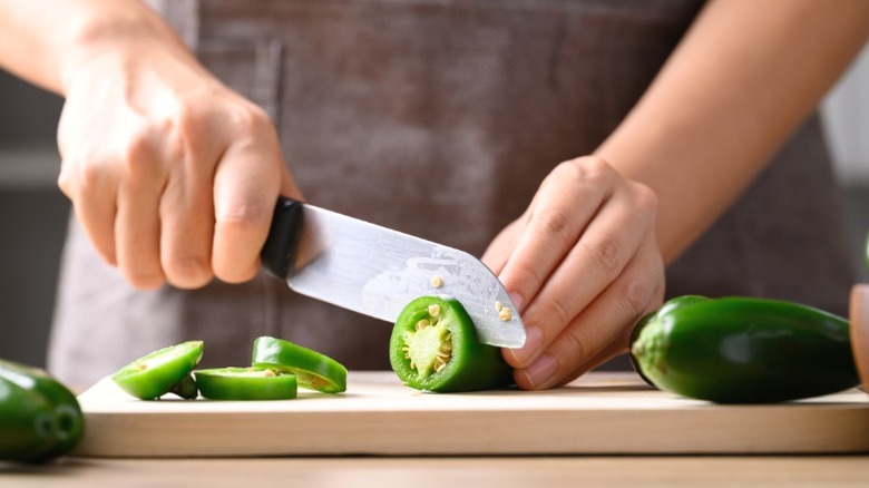 A chef slicing jalapeño peppers on a wooden cutting board.