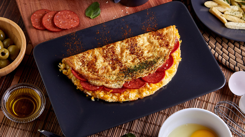 Pepperoni omelet in black plate on wood table.