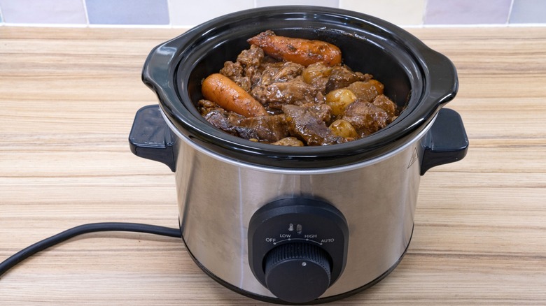 Slow cooker with meat and vegetables on wood counter