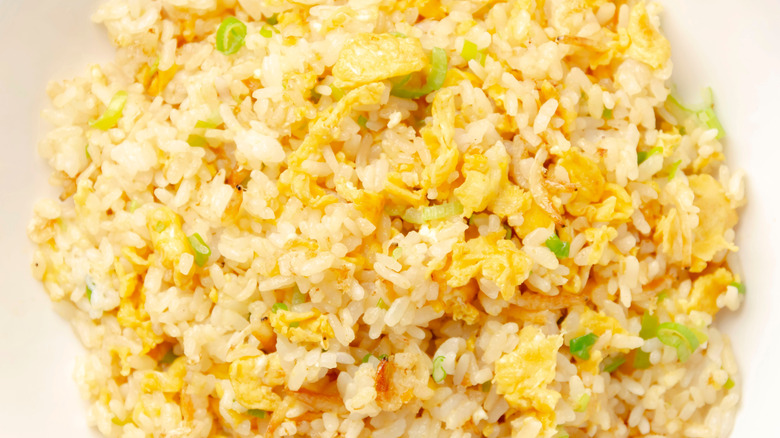 A plate of softly fried rice with eggs and scallions in it.