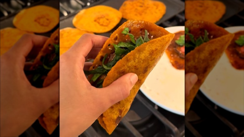 A person holds a sweet potato taco shell filled with lettuce and other taco ingredients