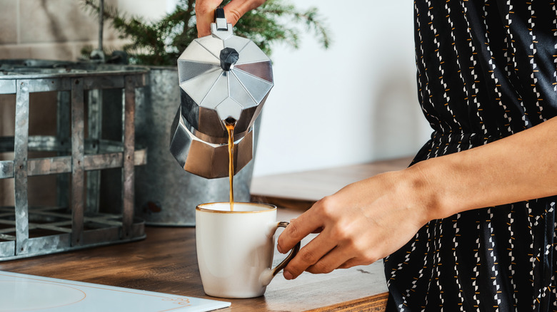 Person pouring coffee into a mug at home.