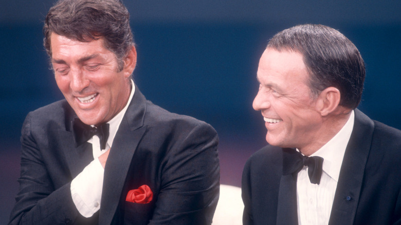 Frank Sinatra sitting next to Dean Martin, both wearing suits and laughing
