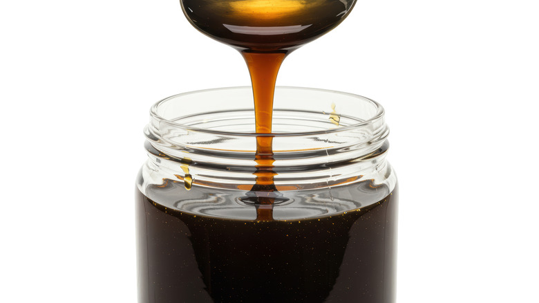 Closeup of molasses pouring from spoon to jar