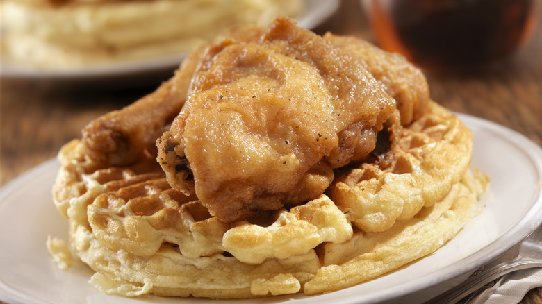 A piece of fried chicken on top of two round waffles on a round white plate