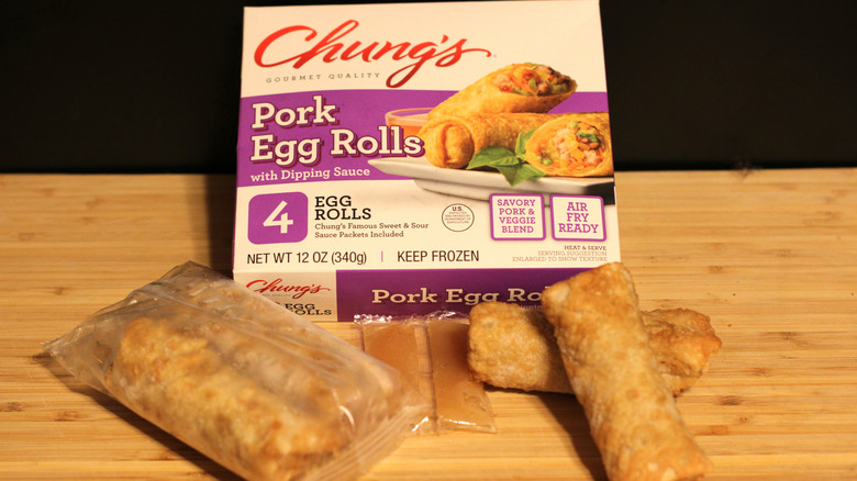 An empty box of Chung's pork egg rolls alongside its contents displayed on a cutting board