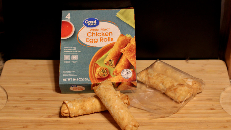 An empty box of Great Value chicken egg rolls alongside its contents displayed on a cutting board