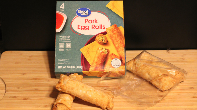 An empty box of Great Value pork egg rolls alongside its contents displayed on a cutting board