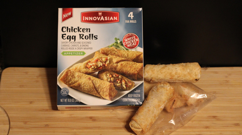 An empty box of InnovAsian chicken egg rolls alongside its contents displayed on a cutting board