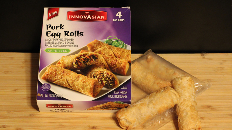An empty box of InnovAsian pork egg rolls alongside its contents displayed on a cutting board