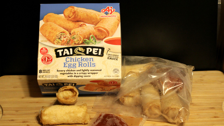 An empty box of Tai Pei chicken egg rolls alongside its contents displayed on a cutting board