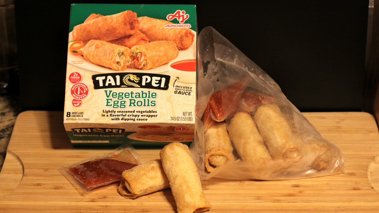 An empty box of Tai Pei vegetable egg rolls alongside its contents displayed on a cutting board