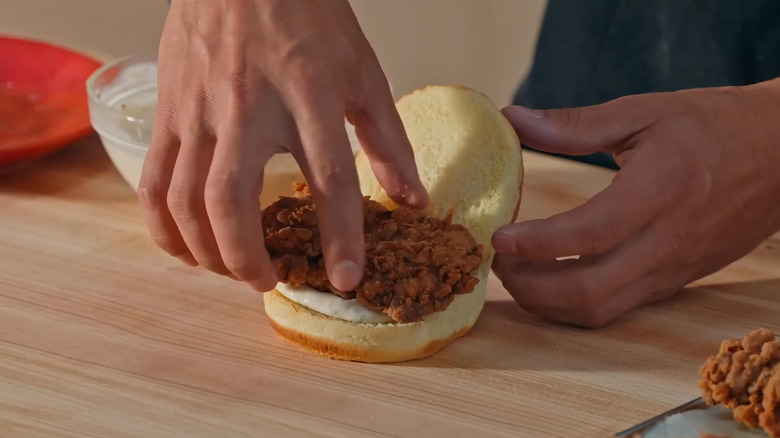 Hand placing fried chicken cutlet on bun with mayo