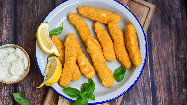 A plate of fish sticks garnished with lemon and served with a bowl of tartar sauce