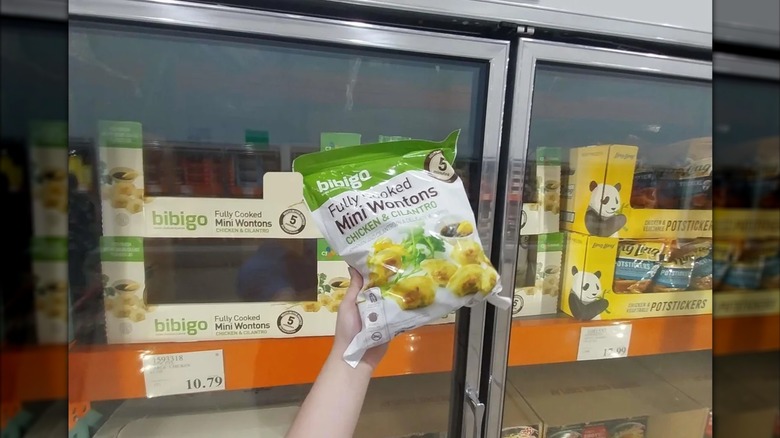 Customer holding bag of Bibigo chicken and cilantro mini wontons in front of freezer aisle at Costco