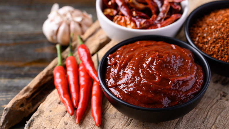 A bowl of gochujang sauce with red chilis on the left of it