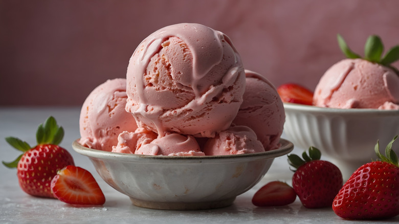 A bowl piled high with strawberry ice cream surrounded by fresh strawberries