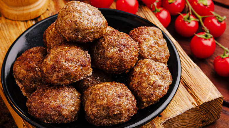 Pile of meatballs in a black bowl next to tomatoes