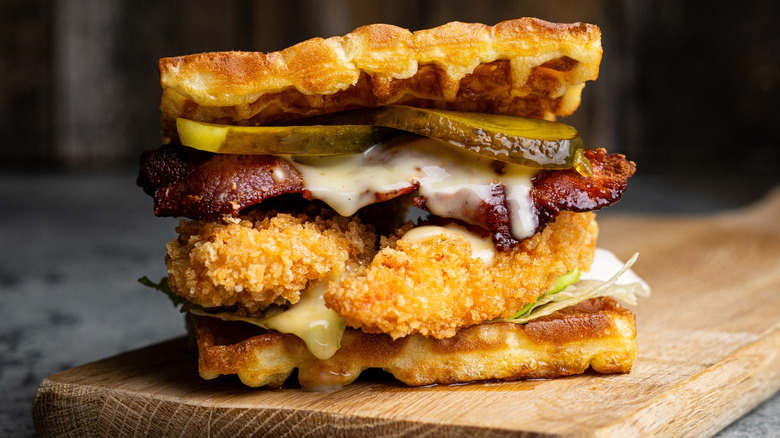 A chicken and waffle sandwich on a wood cutting board